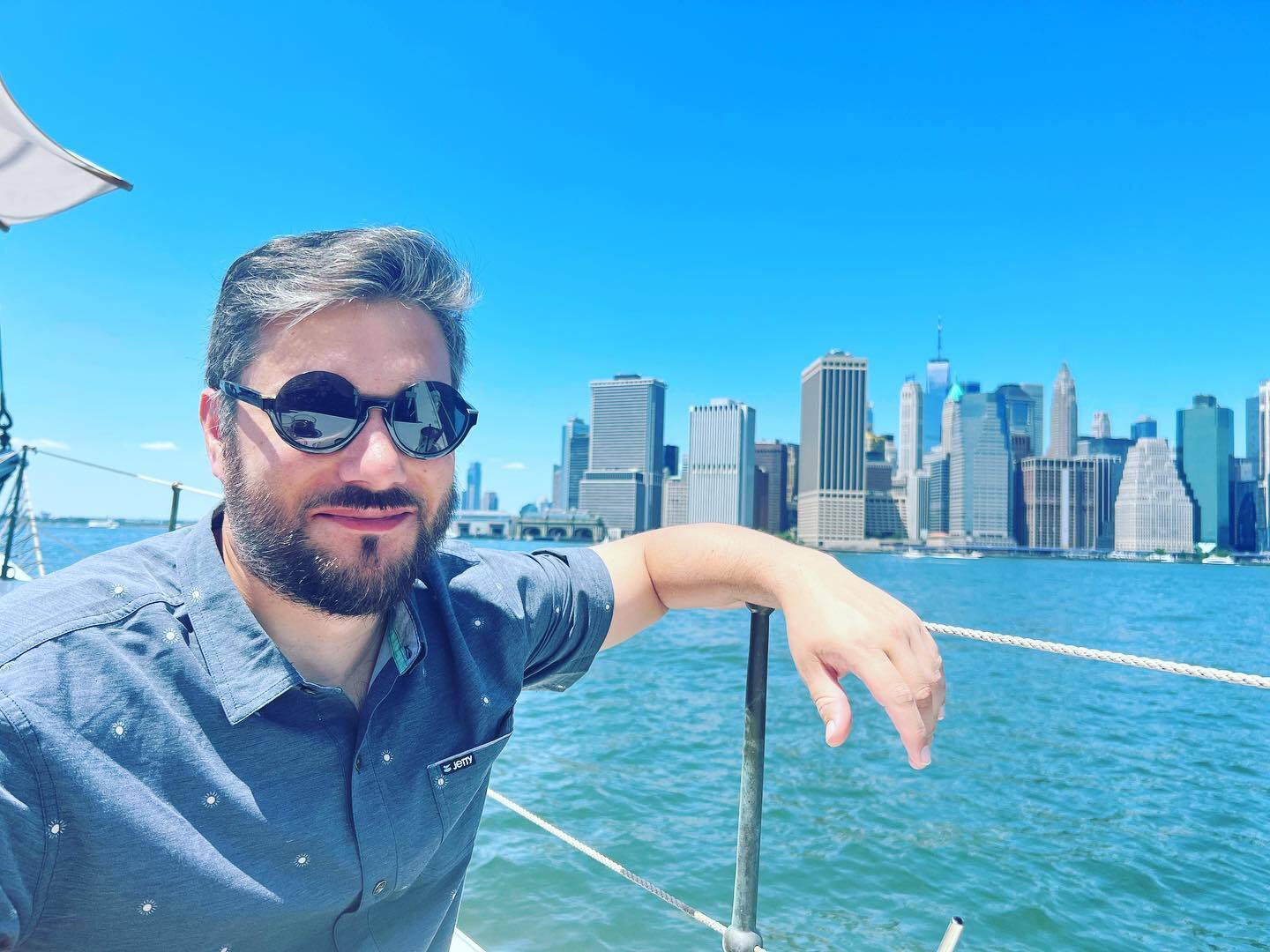 Seorang pria di kacamata hitam duduk di atas perahu di depan cakrawala Manhattan yang lebih rendah