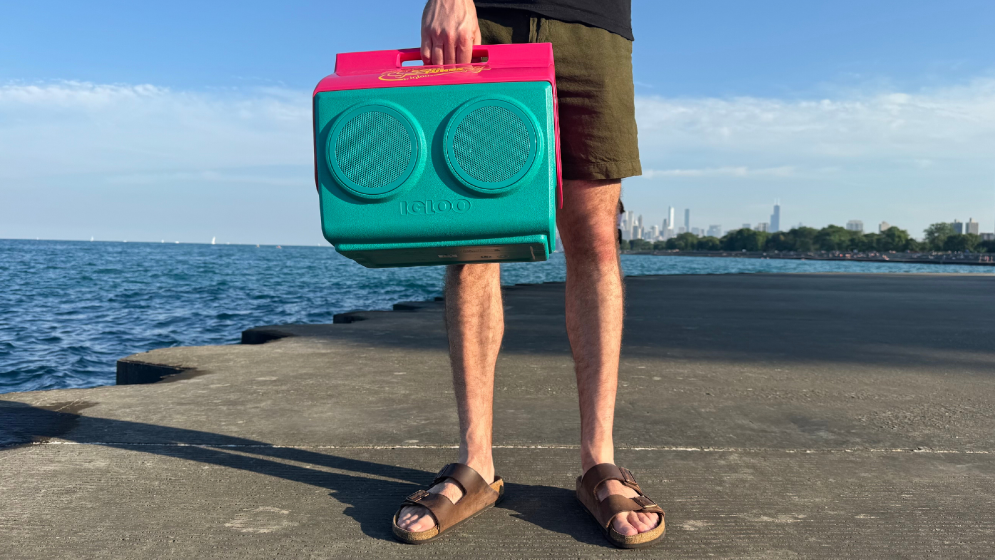 Tampilan dekat seorang pria yang memegang speaker Igloo Kooltunes di tangga beton di dekat danau
