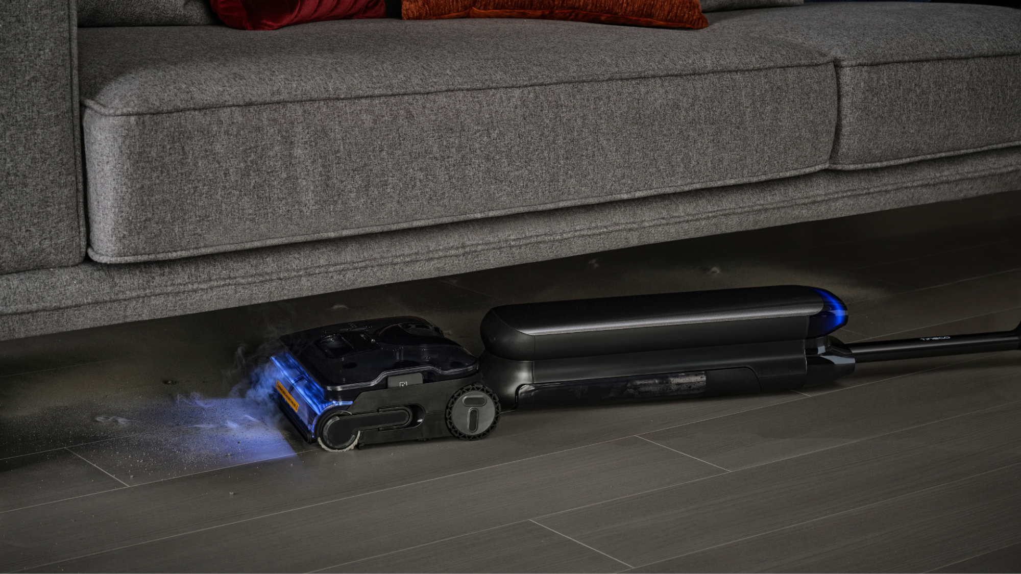 Gambar promosi artis Tineco S9 Steam berbaring rata untuk mengukus di bawah sofa.