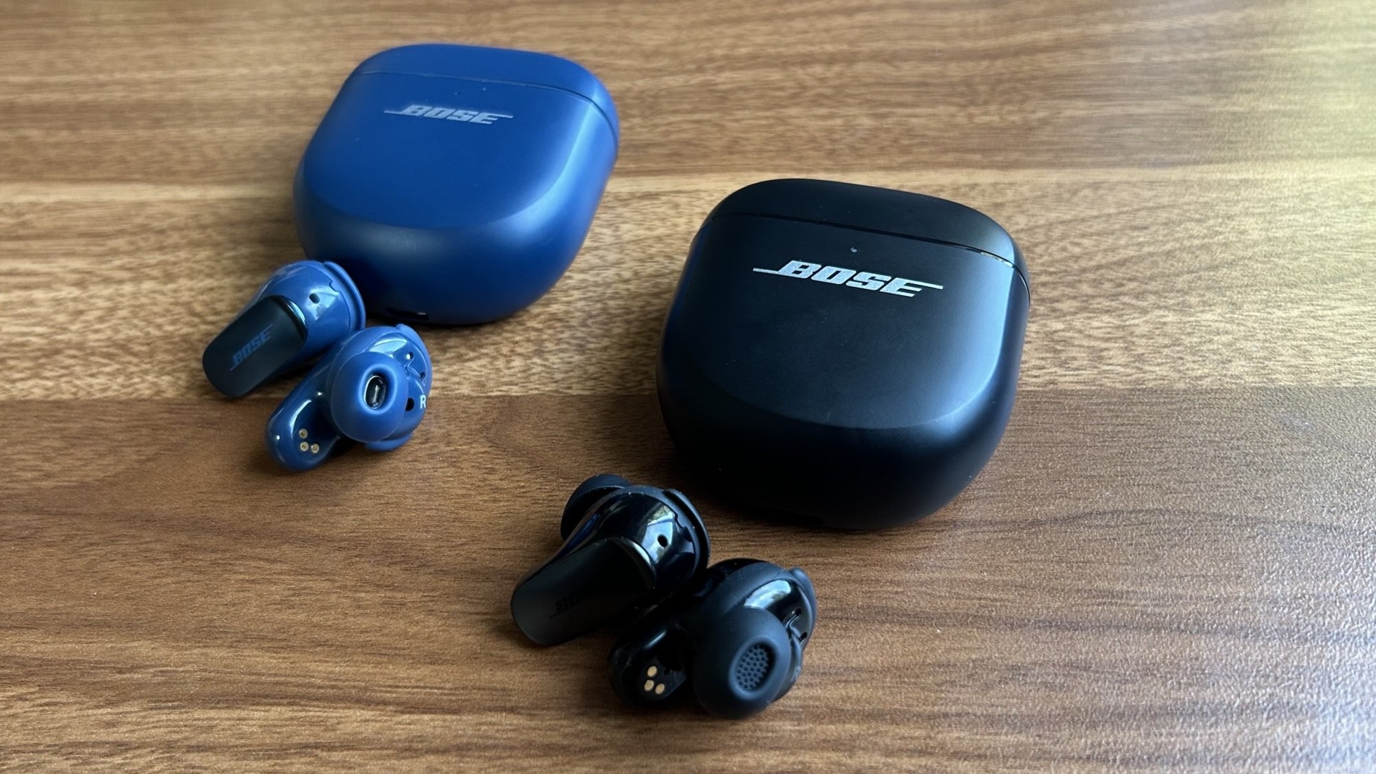 Bose QC Ultra 1 earbud di sebelah earbud QC Ultra 2 di desktop