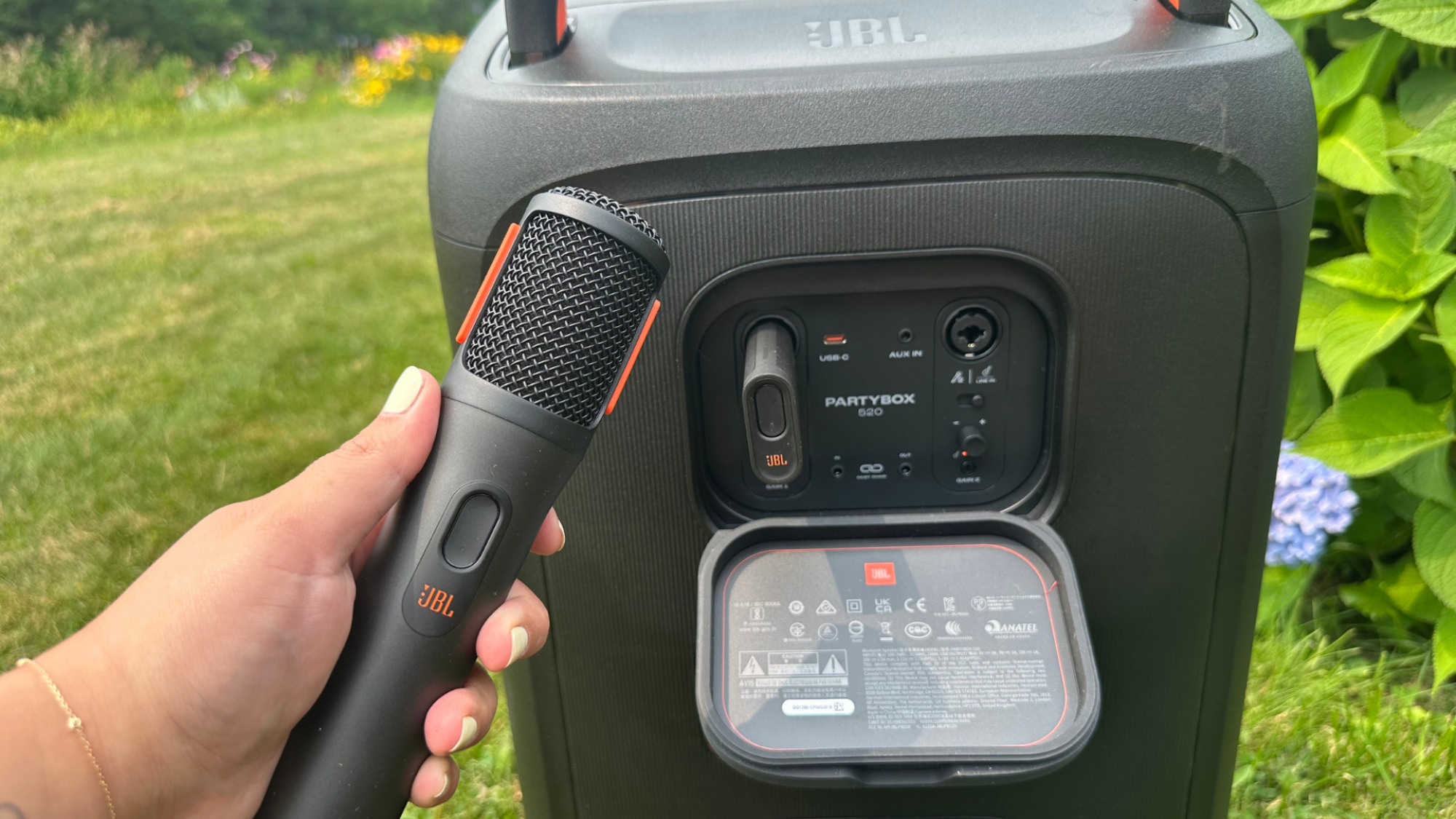 Sisi belakang JBL Partybox 520 dan tangan memegang mikrofon JBL nirkabel.